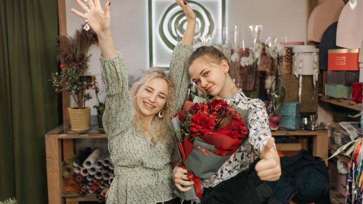 Two happy florists celebrate with a bouquet of red roses in their flower shop.