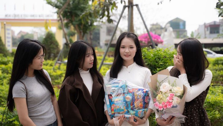 Four young women celebrate outdoors with gifts and flowers.
